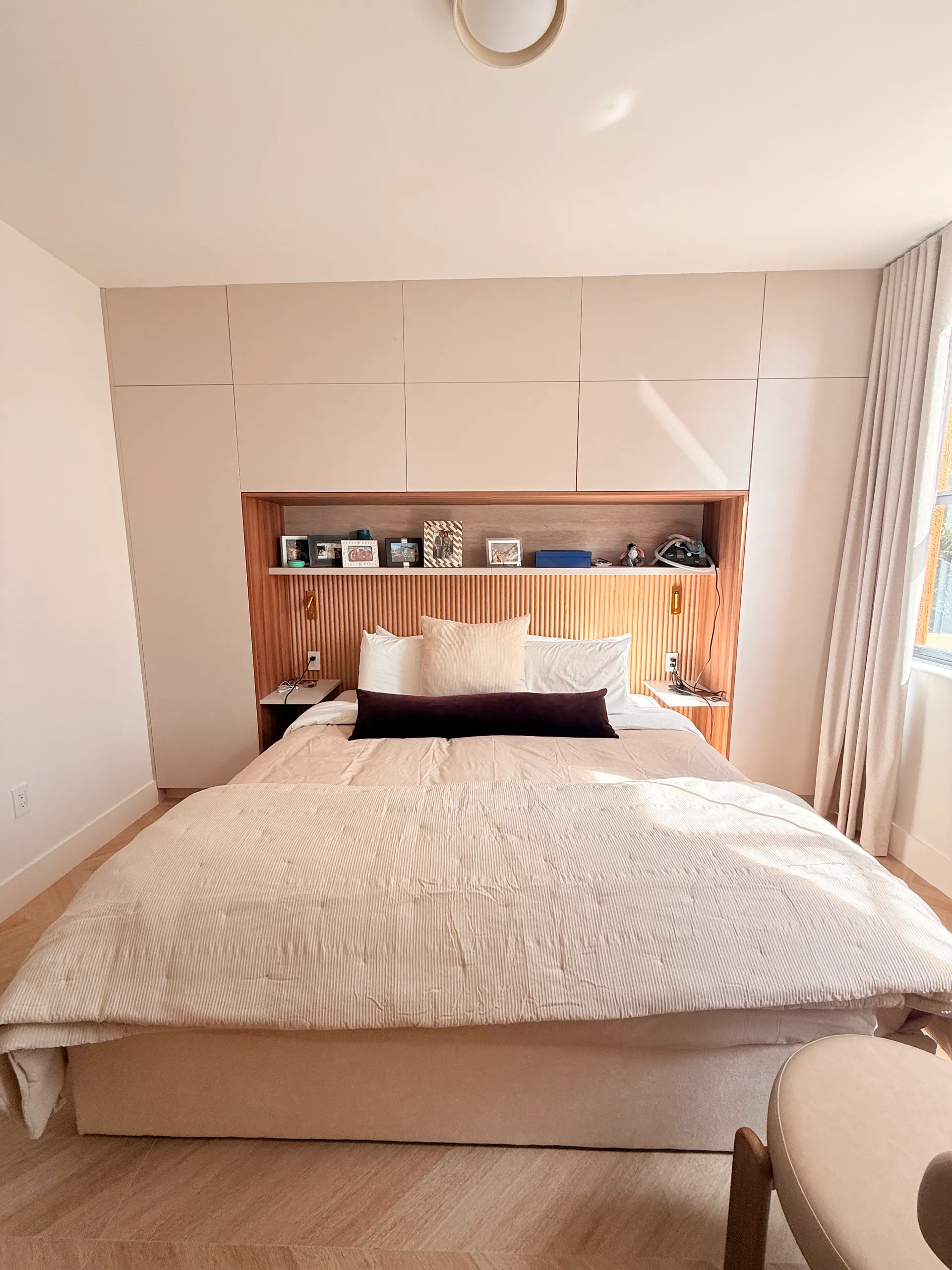 The finished bedroom: bed made against the fluted oak headboard, lit shelf with photos above it and floating nightstands on both sides