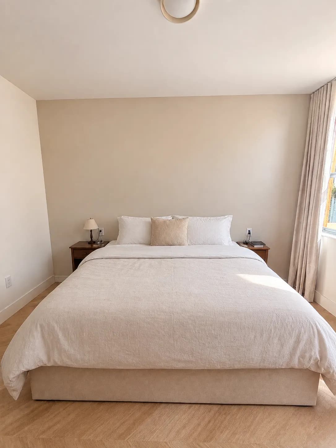 The bedroom before: a bed against a plain beige wall, with two small wooden nightstands and no built-in storage