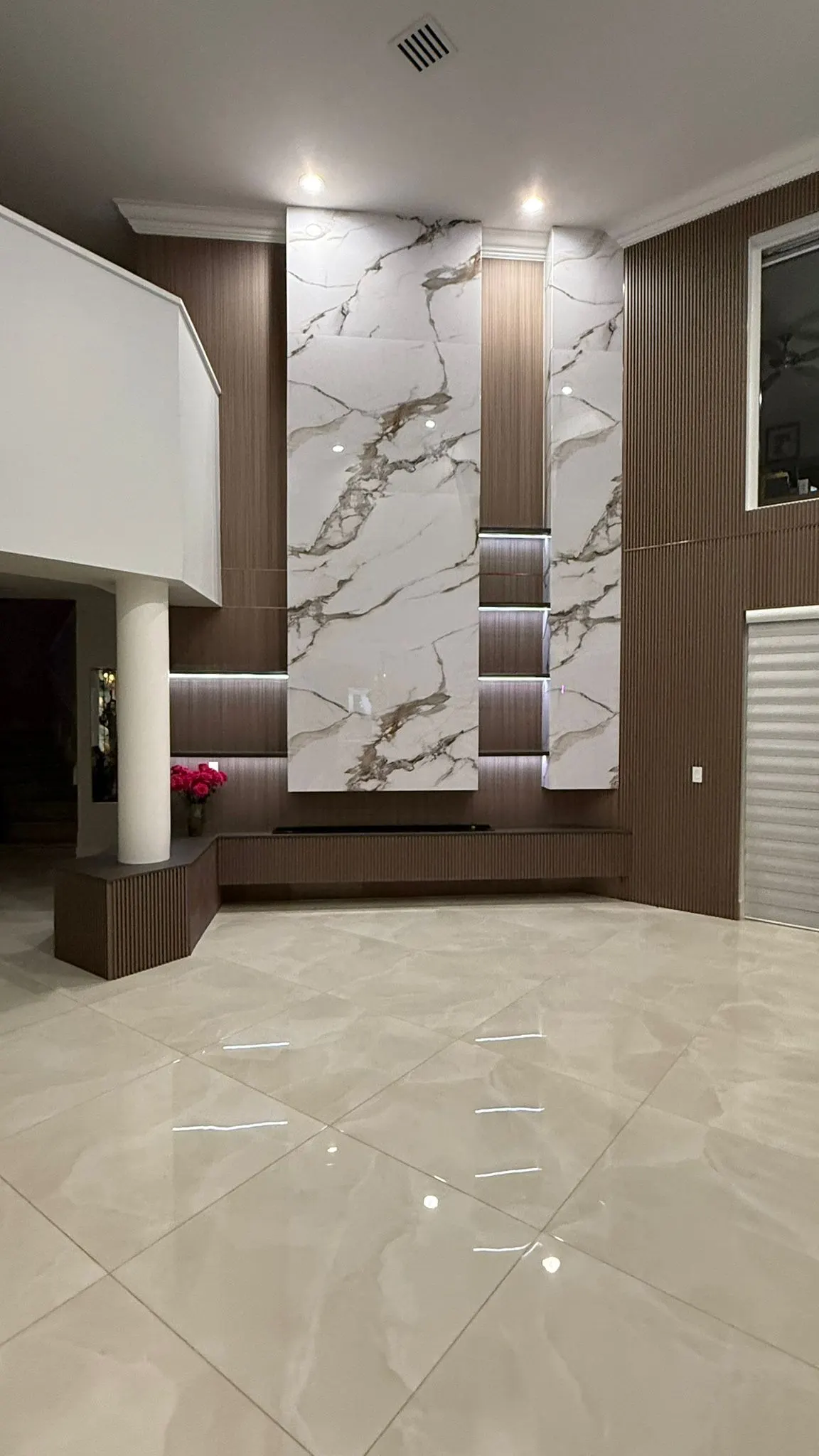The same wall after: marble-look panels and fluted wood floor to ceiling, lit niches and a low fluted console with a linear fireplace