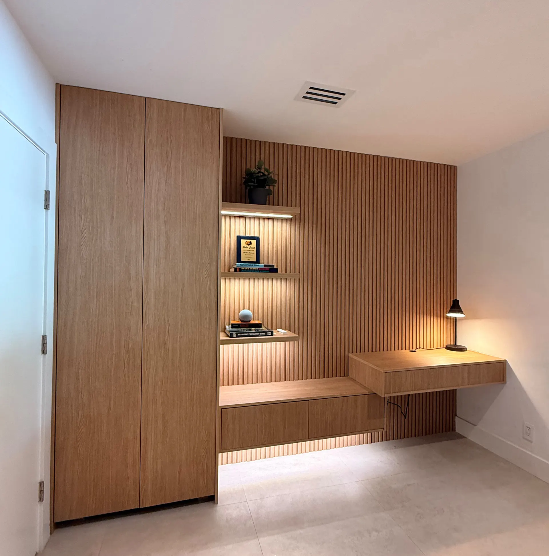 The same wall after: a floor-to-ceiling oak wardrobe, slatted panelling with lit niches and a floating desk