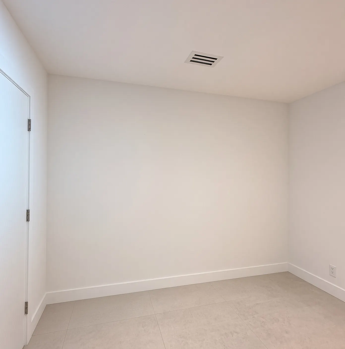 The room before: a bare white wall beside the door, with the ceiling vent and porcelain tile floor