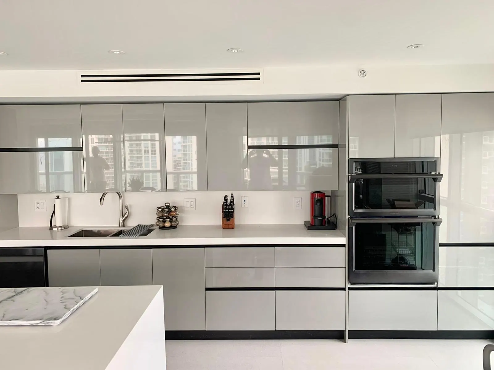 Modern kitchen with grey high-gloss handleless cabinets, a white quartz counter, a double wall oven and a marble-topped island